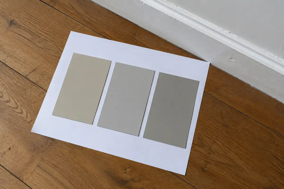 Trois échantillons de beige et de gris posés sur une feuille blanche près d'une plinthe