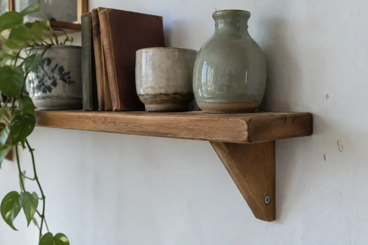 Étagère en bois massif sur équerre, fixée à un mur blanc, avec des pots en céramique et de vieux livres