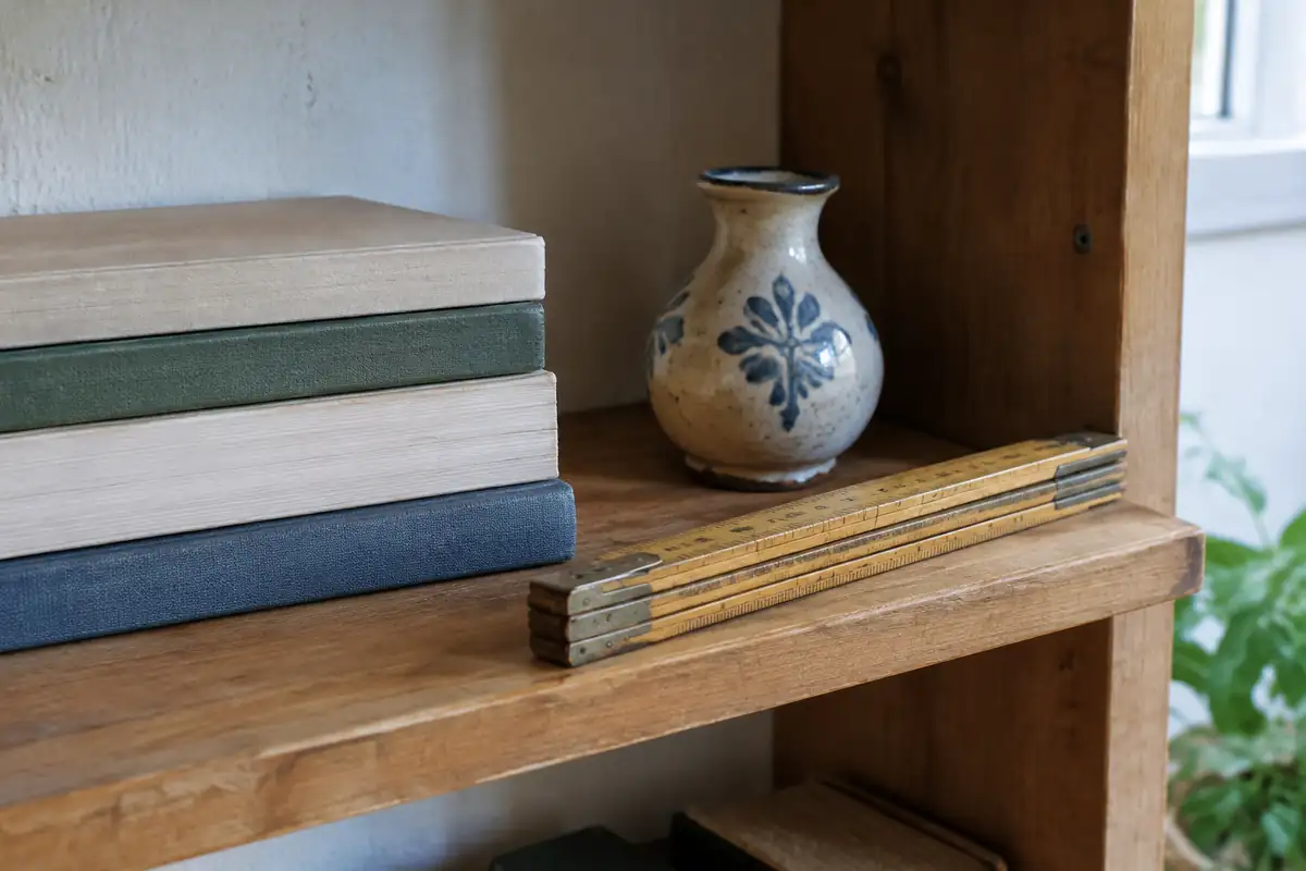 Tablette en bois avec une pile de livres, un petit vase et une règle pliante posée sur le bord